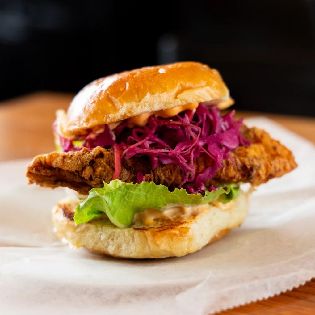 You're My Boy Blue is a fried catfish sandwich decorated with purple cabbage slaw and our delicious house-made kitchen sauce.